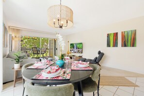 A dining area with a round table, chairs, and a hanging light fixture. - Hale Kamaole 244 - Modern Suite next to Beach (Kihei)
