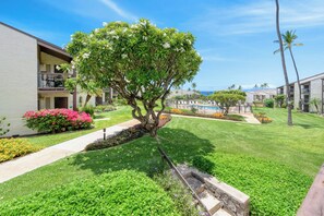 A well-maintained outdoor area with a pool, a tree-lined pathway, and a view of the ocean. - Hale Kamaole 244 - Modern Suite next to Beach (Kihei)