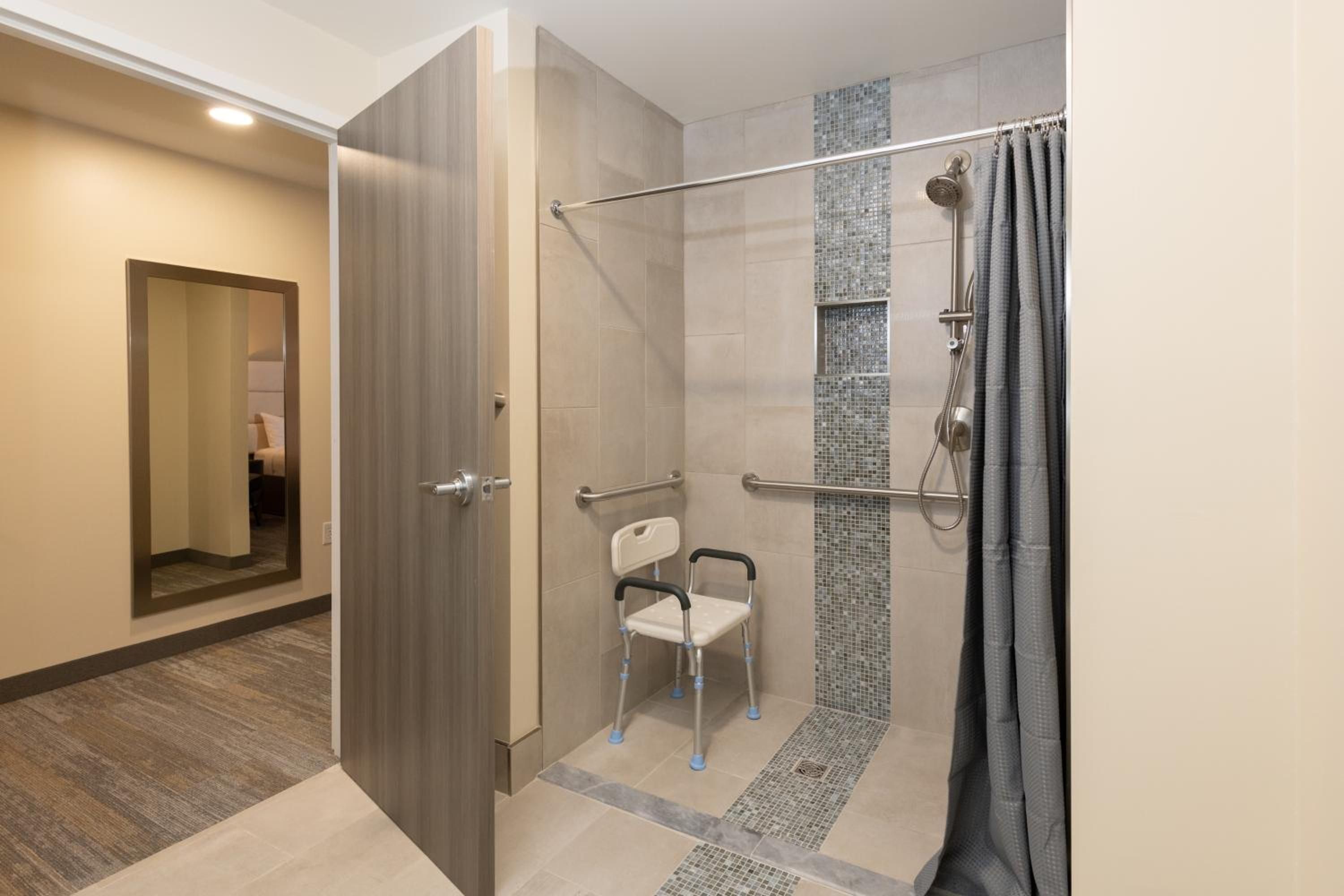Une salle de bain moderne dotée d’une douche à l’italienne, d’une barre d’appui et d’un banc accessible aux personnes en fauteuil roulant.