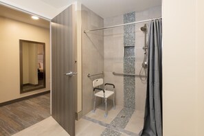Un baño moderno con cabina de ducha, barra de apoyo y banco accesible en silla de ruedas.