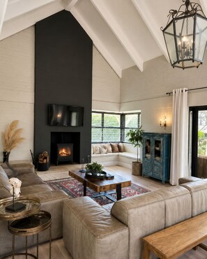 A spacious living room with a fireplace, leather sofas, a wooden coffee table, and a large window with blinds. - 10 sleeper villa with daily housekeeper -near vineyard (Cape Town)