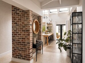 A modern interior with a brick accent wall, a round mirror, a dining area with bar stools, and a glass cabinet with various items. - 10 sleeper villa with daily housekeeper -near vineyard (Cape Town)