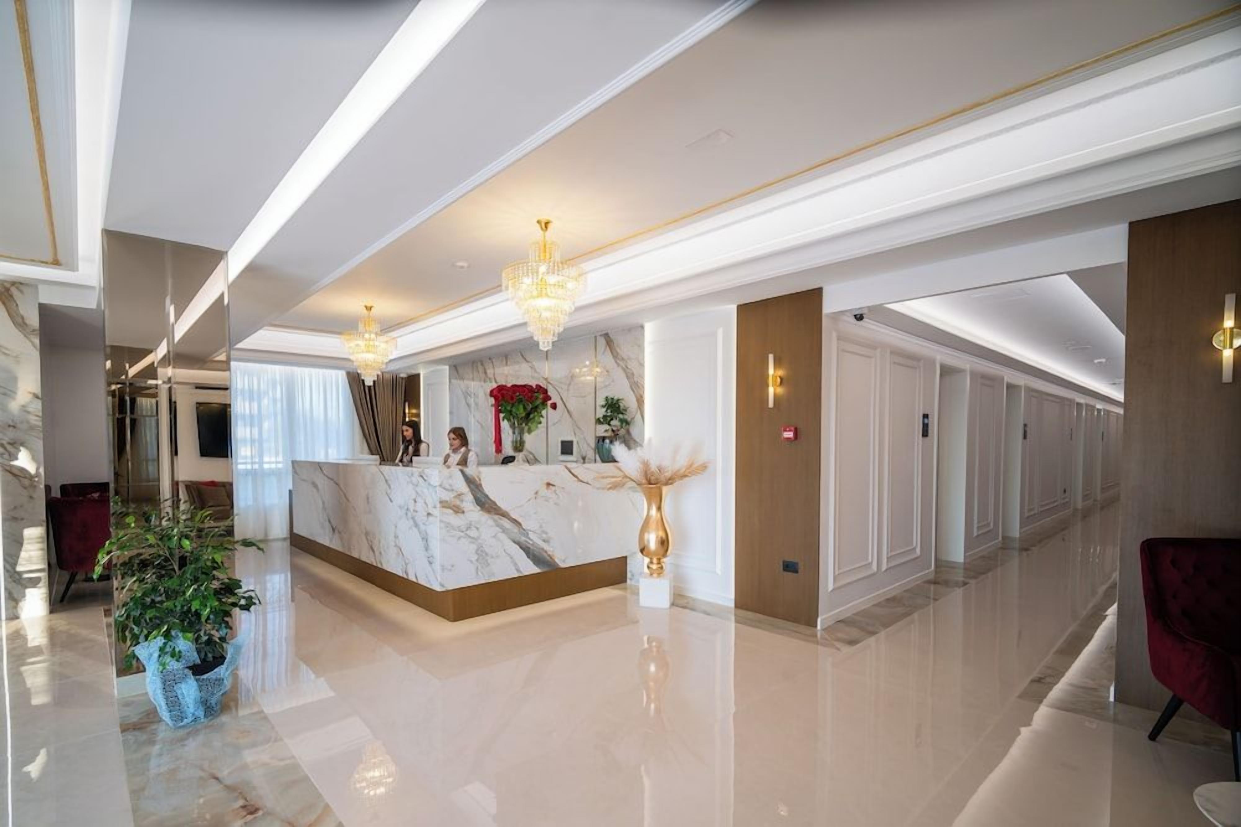 Zona de recepción de hotel con mostrador de mármol, candelabros y una silla roja.