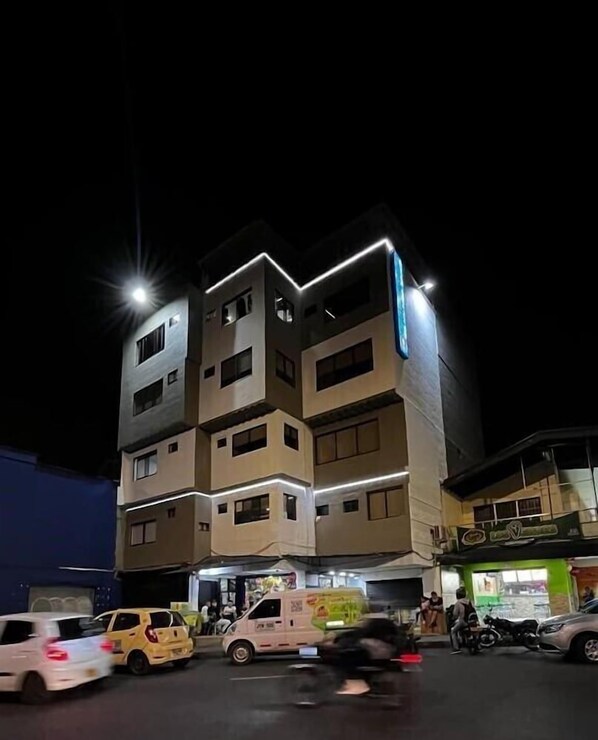 A multi-story building with illuminated signage, a parking area with vehicles, and a storefront with a green awning. - 33hotel (Medellín)