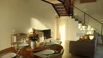 A dining area with a round table set for four, a sofa, and a staircase leading to an upper level.