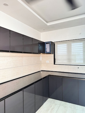 Een moderne keuken met zwarte kastjes, een marmeren aanrechtblad en een raam met jaloezieën.