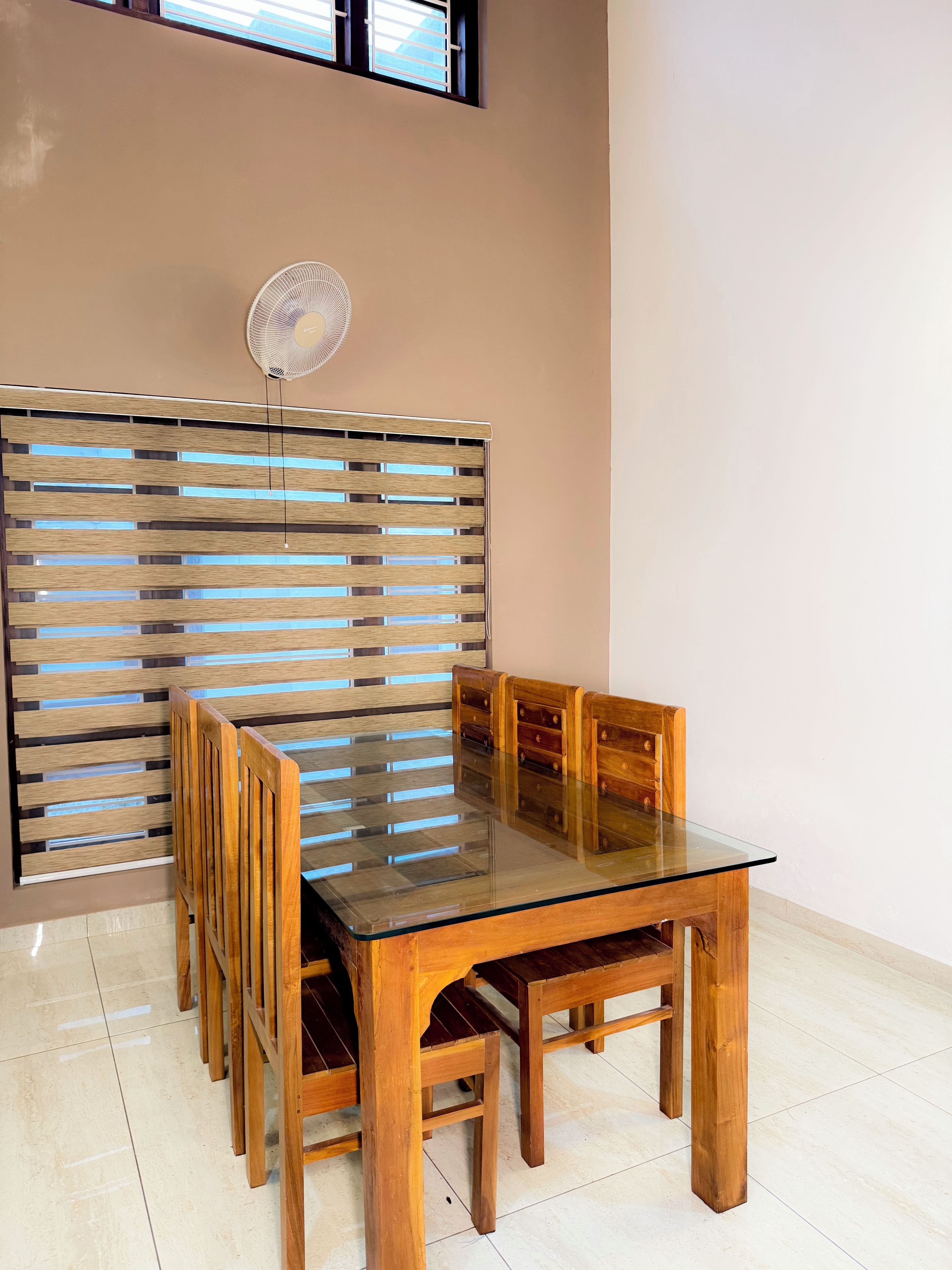 Un comedor con una mesa de vidrio, sillas de madera, un separador de listones de madera y un ventilador de techo.