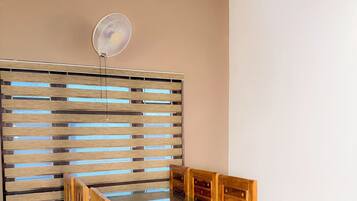Un comedor con una mesa de vidrio, sillas de madera, un separador de listones de madera y un ventilador de techo.