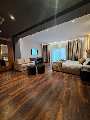 A modern living room with a sofa, ottoman, and a flat-screen TV mounted on the wall. - Olivia Hill Resort (Durrës)