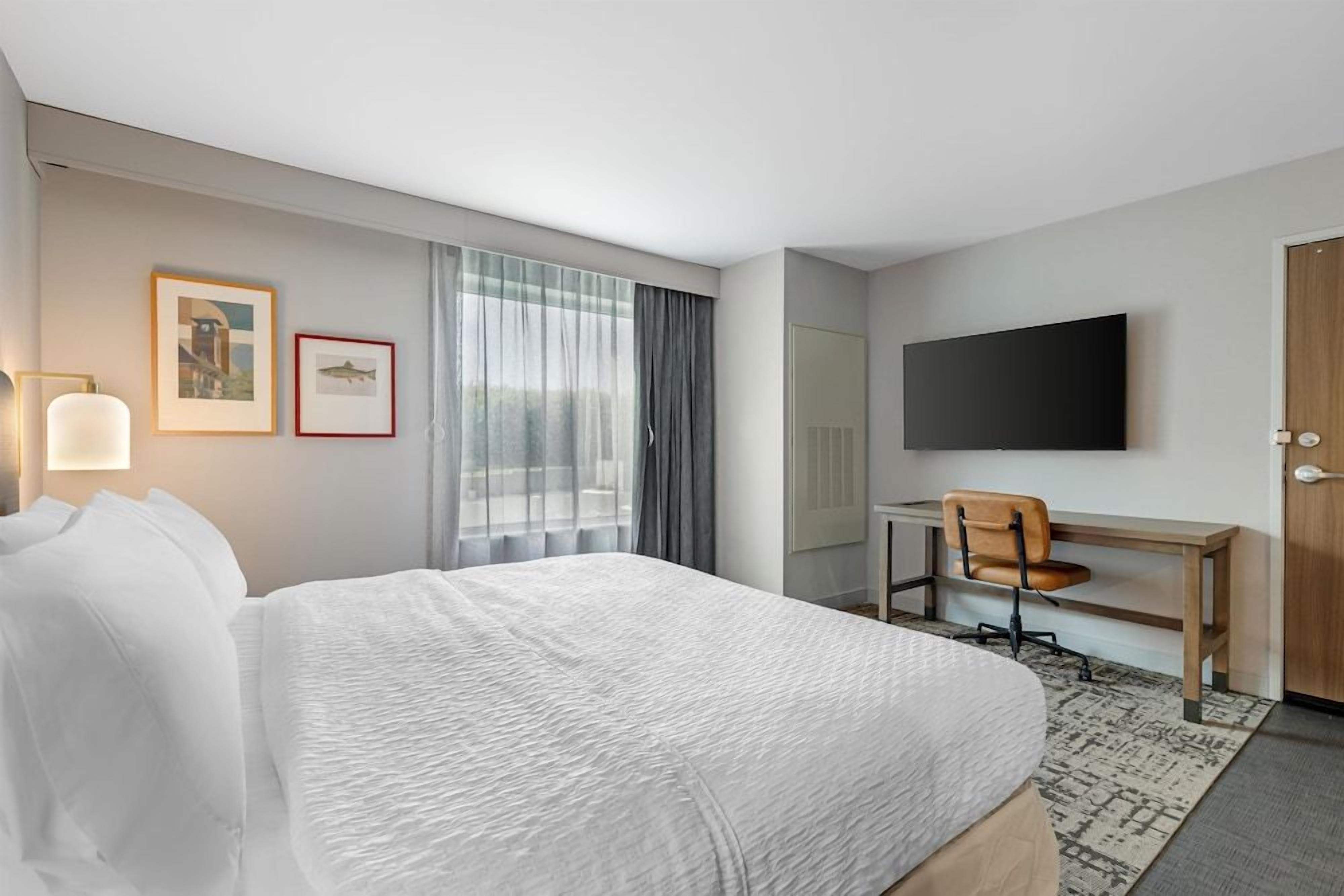 A hotel room with a bed, a desk, a chair, a television, and a window with curtains.