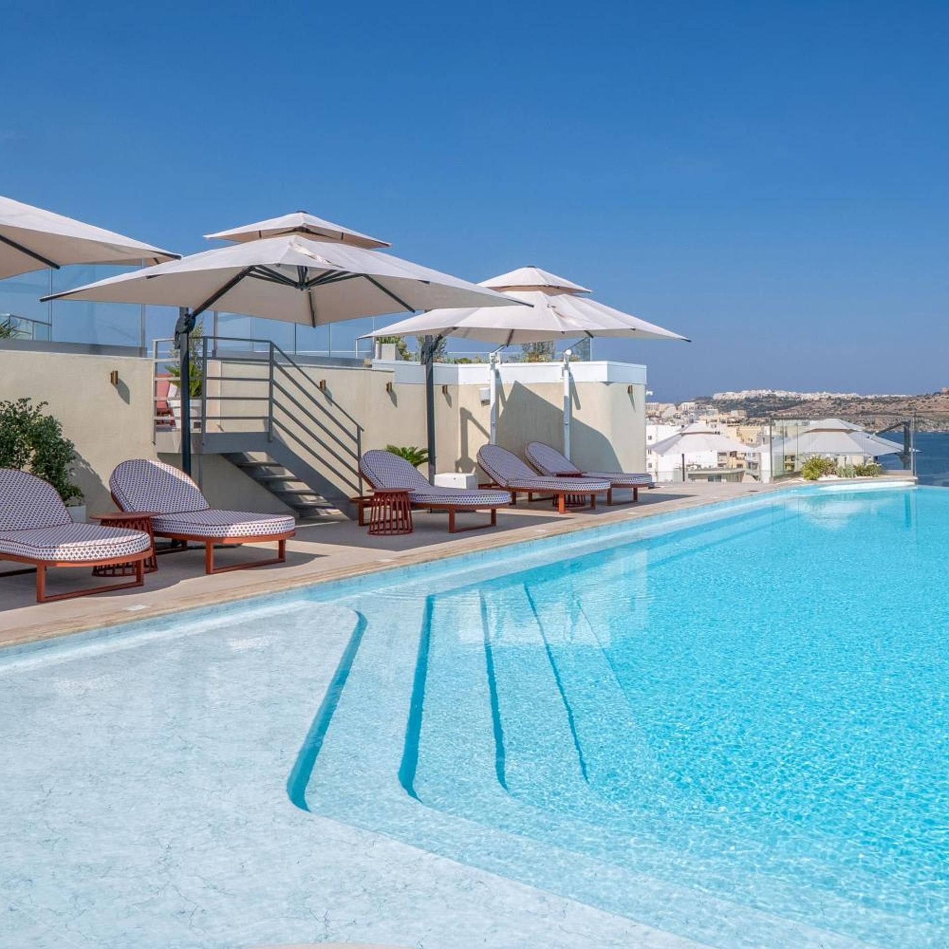 A pool area with lounge chairs and umbrellas, a staircase, and a view of the sea.
