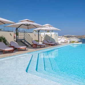A pool area with lounge chairs and umbrellas, a staircase, and a view of the sea. - Innside Bugibba (Malta)