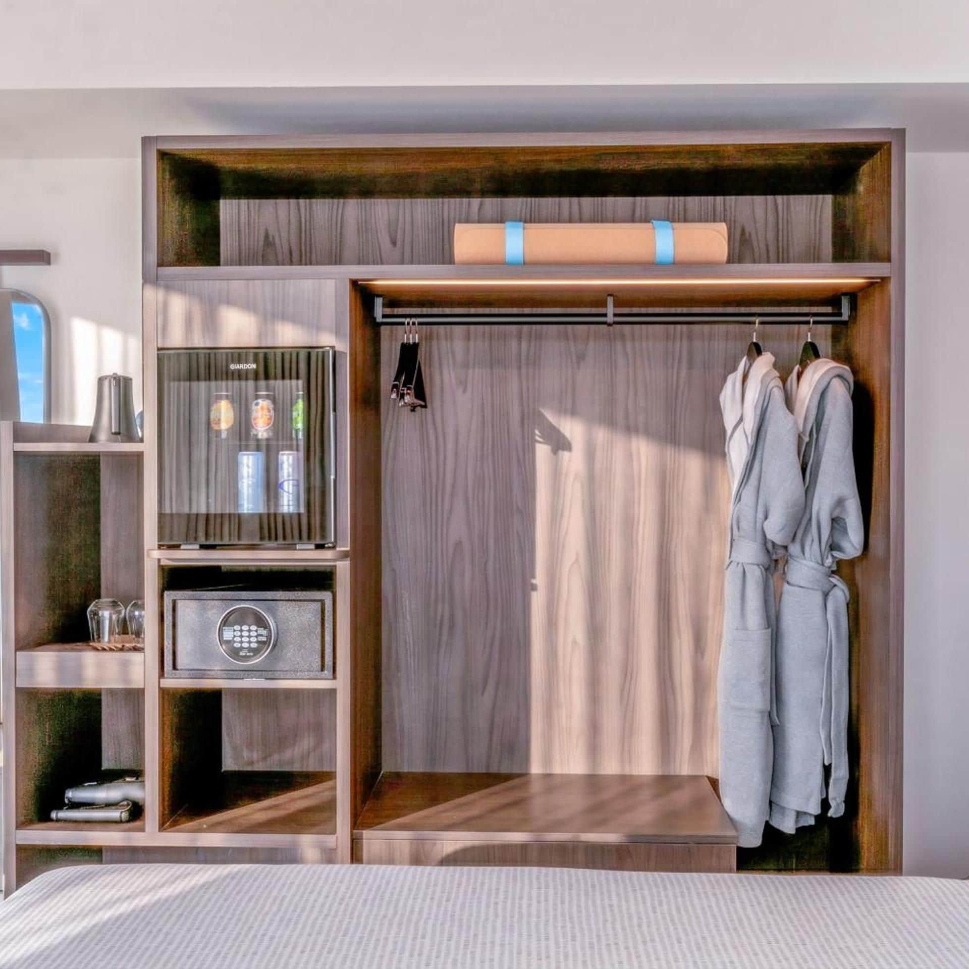 A modern bedroom with a built-in wardrobe, a minibar, and a view of the outdoors.