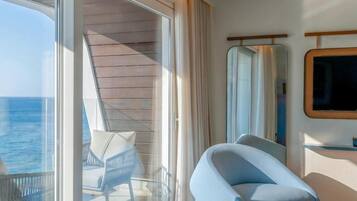 A modern room with a large sliding glass door leading to a balcony, a comfortable chair, a flat-screen TV mounted on the wall, and a bed.