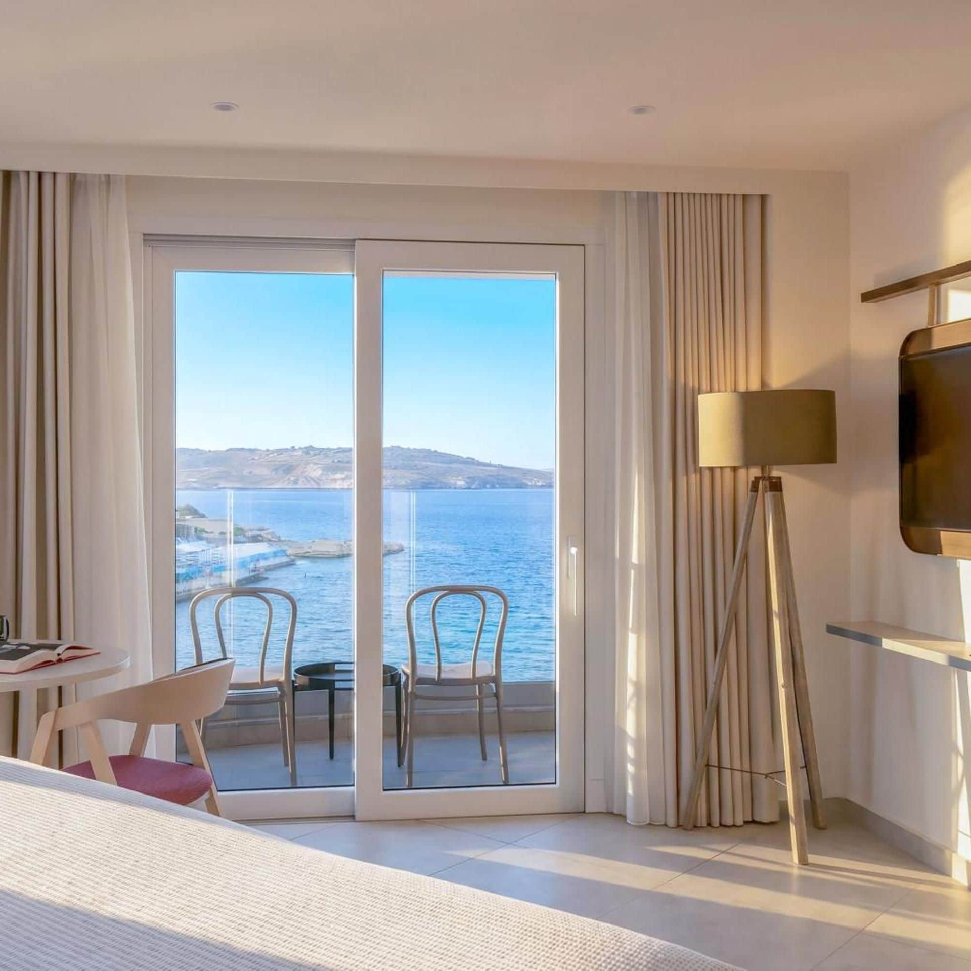 A hotel room with a large sliding glass door leading to a balcony with a view of the sea.