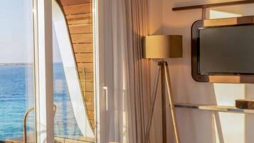 Quarto de hotel com uma janela ampla, televisão de tela plana, abajur e uma mesa com cadeira.