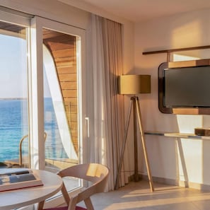 A hotel room with a large window, a flat-screen TV, a floor lamp, and a table with a chair.