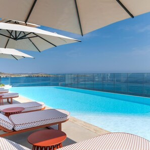 Un espace piscine doté de chaises longues et de parasols, avec vue sur une mer d’un bleu limpide.