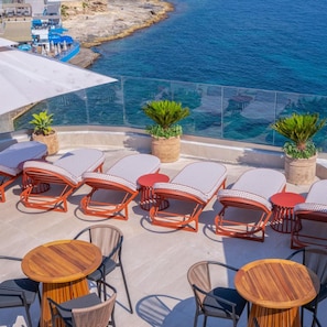 A sunlit outdoor seating area with lounge chairs and tables, overlooking a coastal landscape. - Innside Bugibba (Malta)