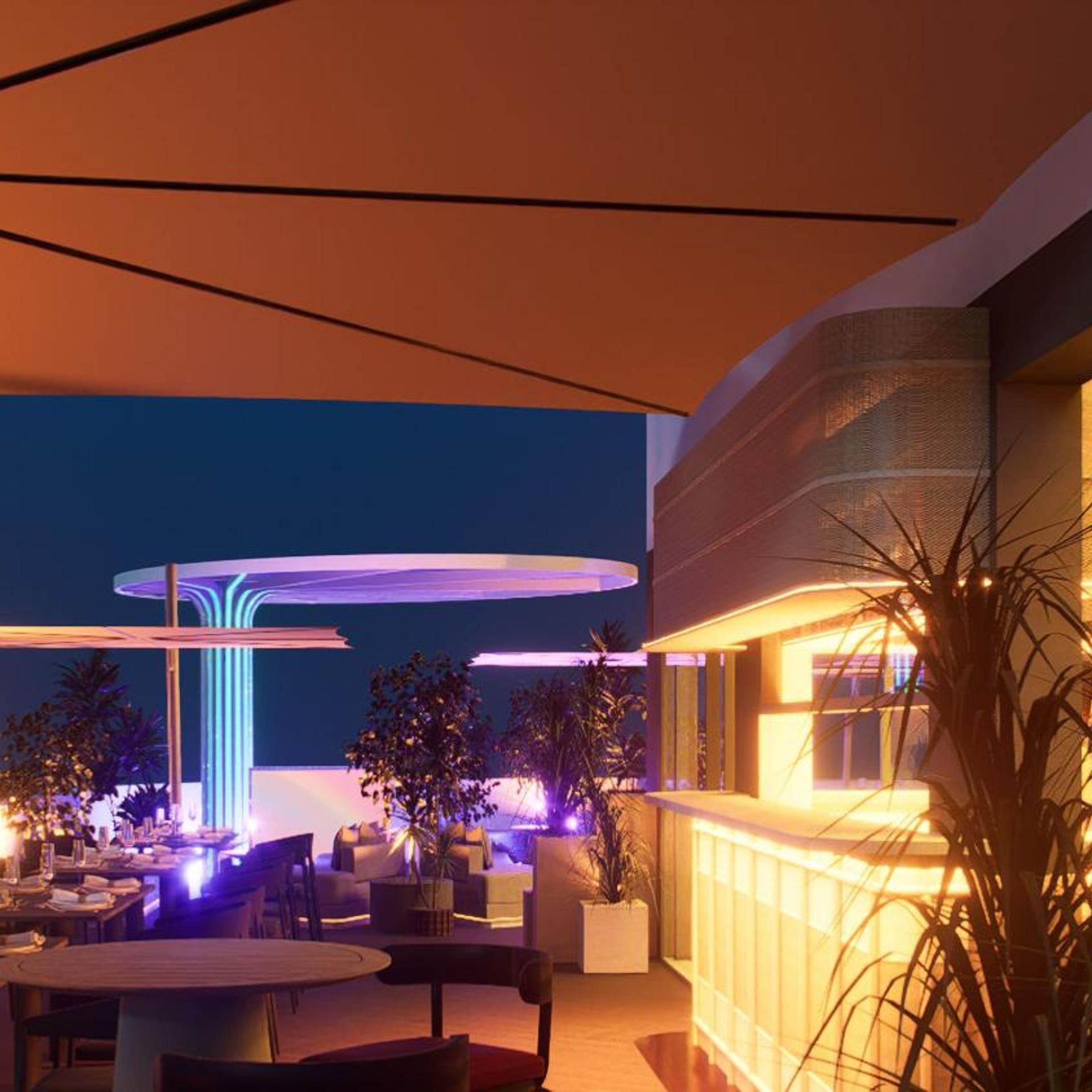 An outdoor dining area with tables and chairs, a modern building with a curved facade, and a decorative light feature.
