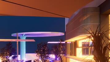 An outdoor dining area with tables and chairs, a modern building with a curved facade, and a decorative light feature.