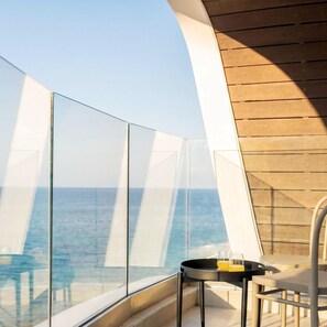 Un balcone con ringhiera in vetro, un tavolo con due bicchieri e vista sull'oceano.