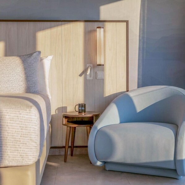 Una habitación de hotel moderna con una cama, una mesita con una taza y un sillón de color claro.