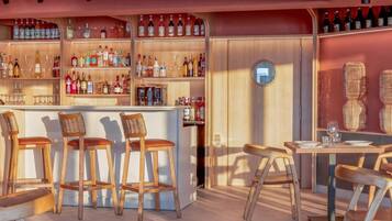 Uma área de bar com banquetas de madeira e balcão, prateleiras com garrafas e um espelho redondo na parede.