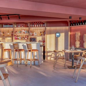 A bar area with wooden stools and a bar counter, shelves with bottles, and a round mirror on the wall.