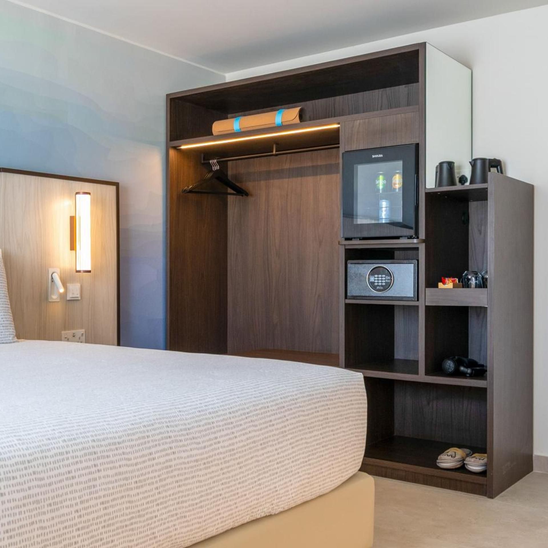 Habitació d'hotel amb llit, armari amb televisió, nevera minibar i prestatge per a sabates.