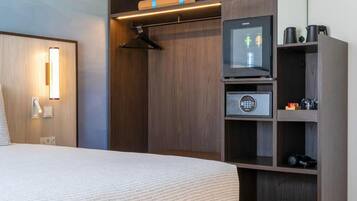 Habitació d'hotel amb llit, armari amb televisió, nevera minibar i prestatge per a sabates.