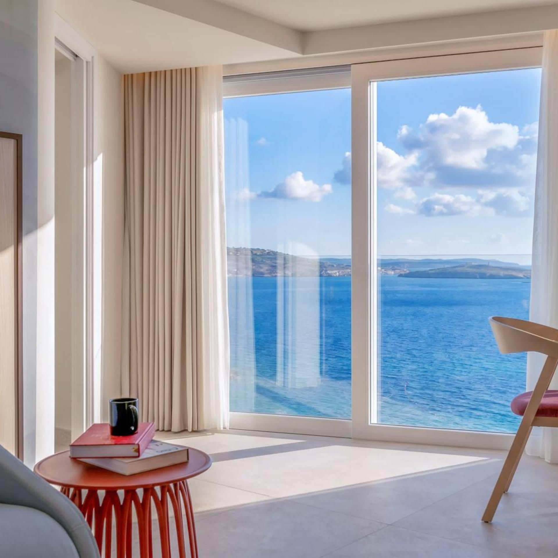 Una habitación moderna con un amplio ventanal corredero que da a un balcón con vistas al mar.