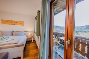 Ein Schlafzimmer mit einem Bett, einem Nachttisch, einer Lampe und Blick auf einen Balkon mit Tisch und Stühlen.
