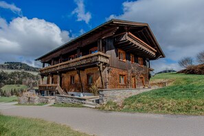Eine traditionelle Holzchalet mit Balkon, eingebettet in einen Hügel unter blauem Himmel.