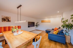 Uma sala de estar moderna com uma mesa de jantar de madeira, sofá azul e uma planta em vaso.