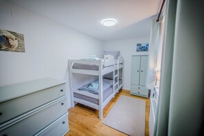 Quarto com beliches, cômoda, armário e radiador.