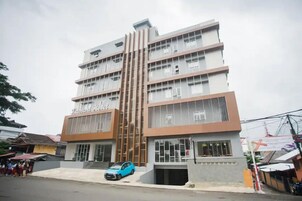 Un hotel de varios pisos con fachada moderna, entrada visible y un automóvil estacionado frente a él.