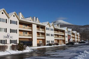 Un hôtel de style nordique doté de nombreux balcons, avec une montagne enneigée en arrière-plan et un ciel dégagé.