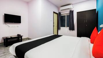 A hotel room with a bed, a flat-screen TV, an air conditioning unit, a desk with a phone, and a wardrobe.