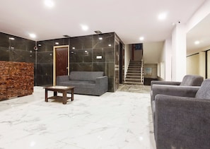 A lobby with a reception desk, grey sofas, a wooden coffee table, and a staircase leading to an upper floor. - Capital O Che Sigma Hotel (Hyderabad)