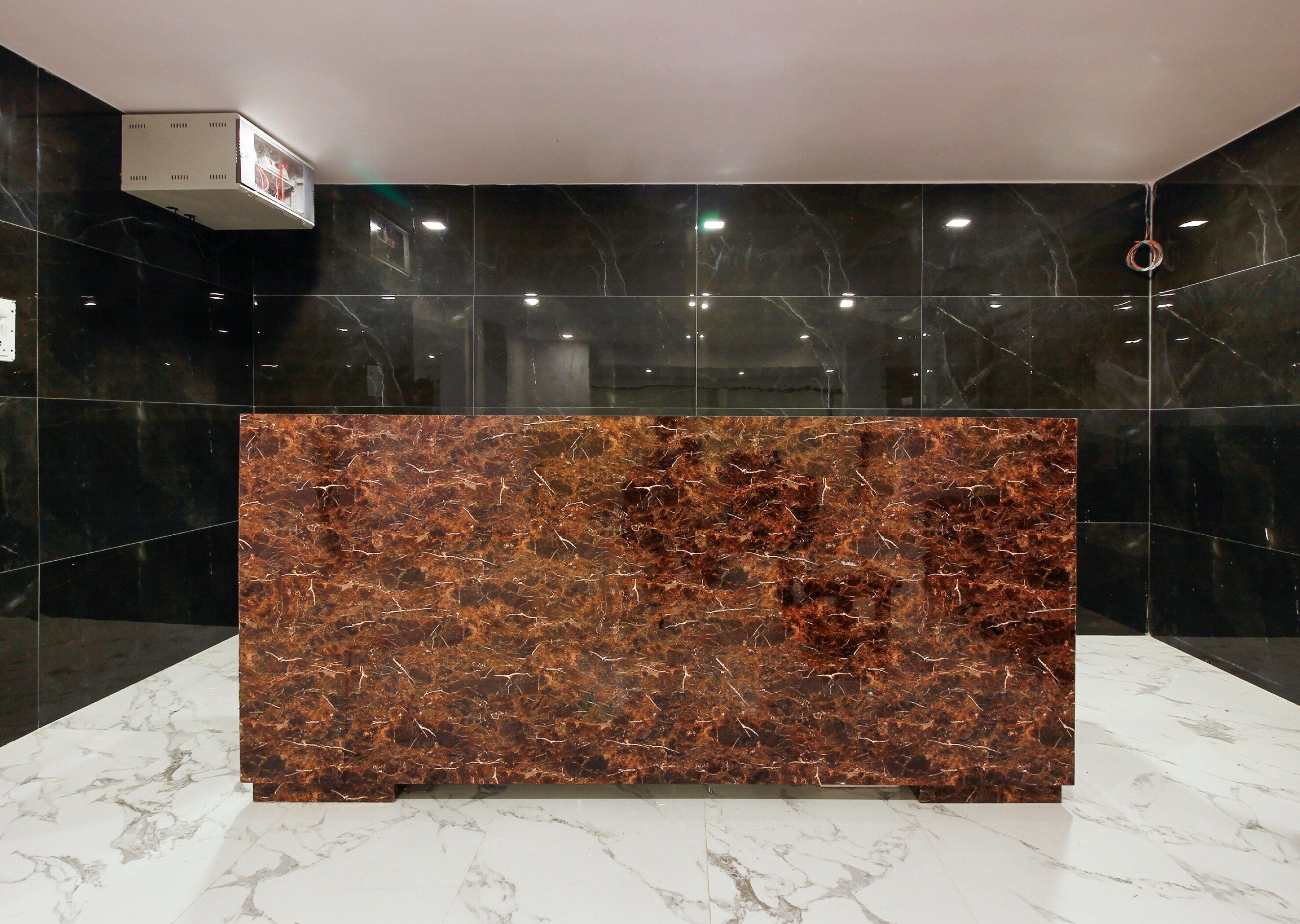 Un mostrador de recepción con encimera de mármol, rodeado de paredes con azulejos negros y un suelo de mármol blanco.