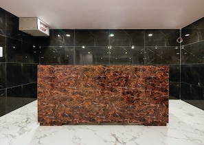 A reception desk with a marble top, surrounded by black-tiled walls and a white marble floor. - Capital O Che Sigma Hotel (Hyderabad)