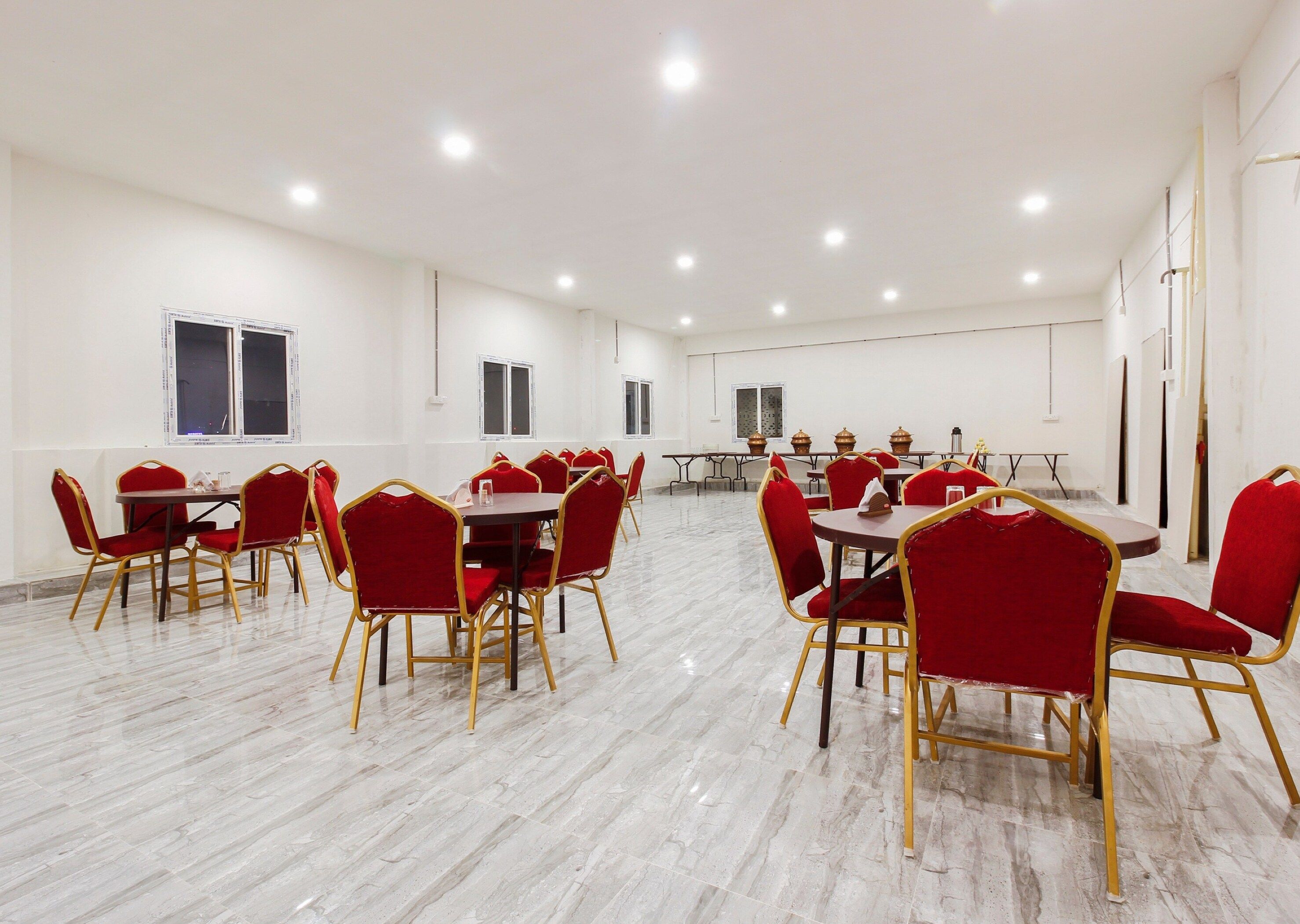 Un salón de conferencias amplio con varias mesas y sillas, paredes blancas y piso de mármol.