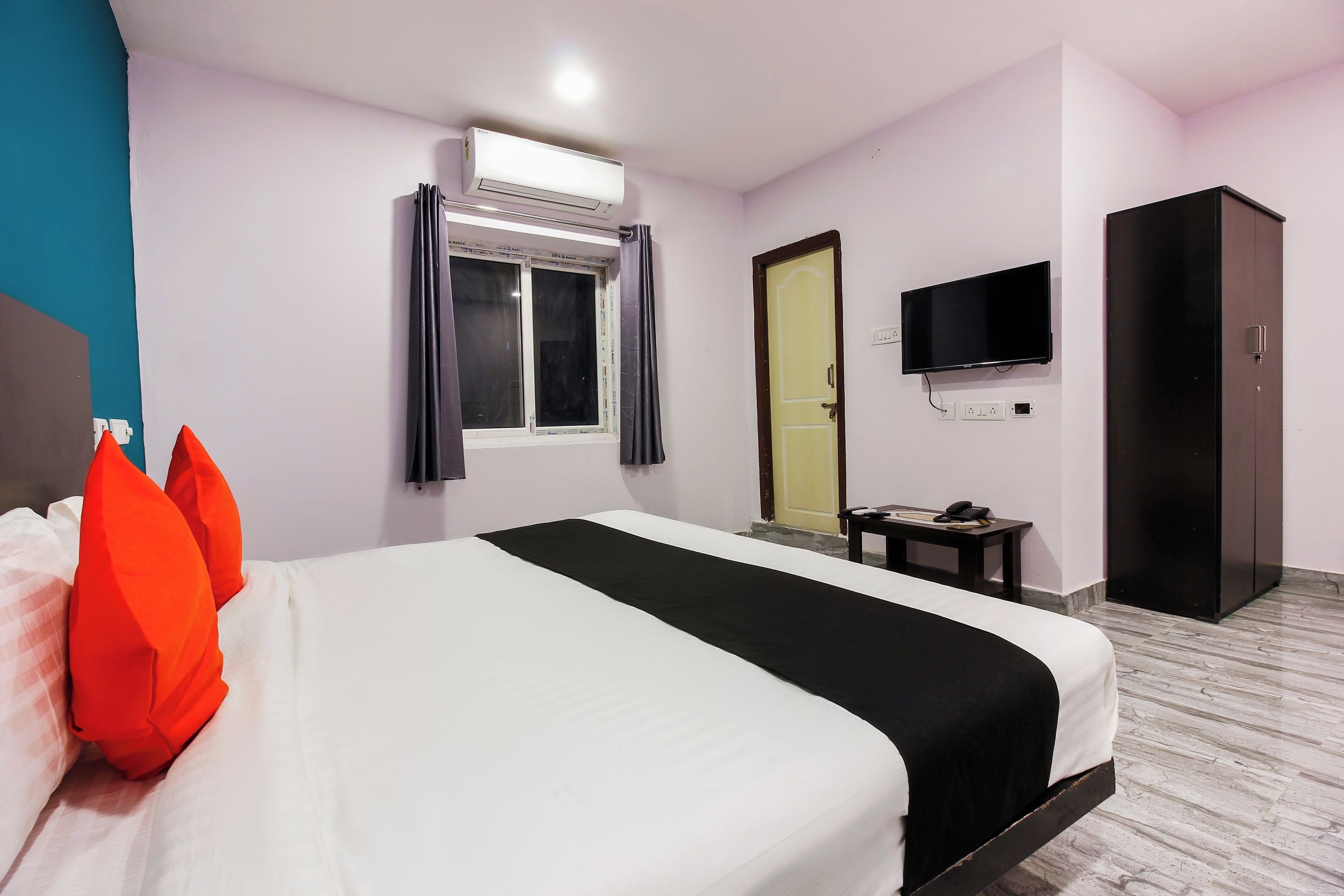 A hotel room with a bed, a television, a wardrobe, and a window with curtains.
