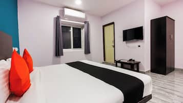 A hotel room with a bed, a television, a wardrobe, and a window with curtains.