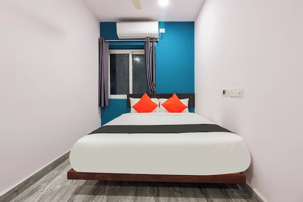 A hotel room with a bed, a window with curtains, an air conditioning unit, and a wall-mounted electrical outlet. - Capital O Che Sigma Hotel (Hyderabad)