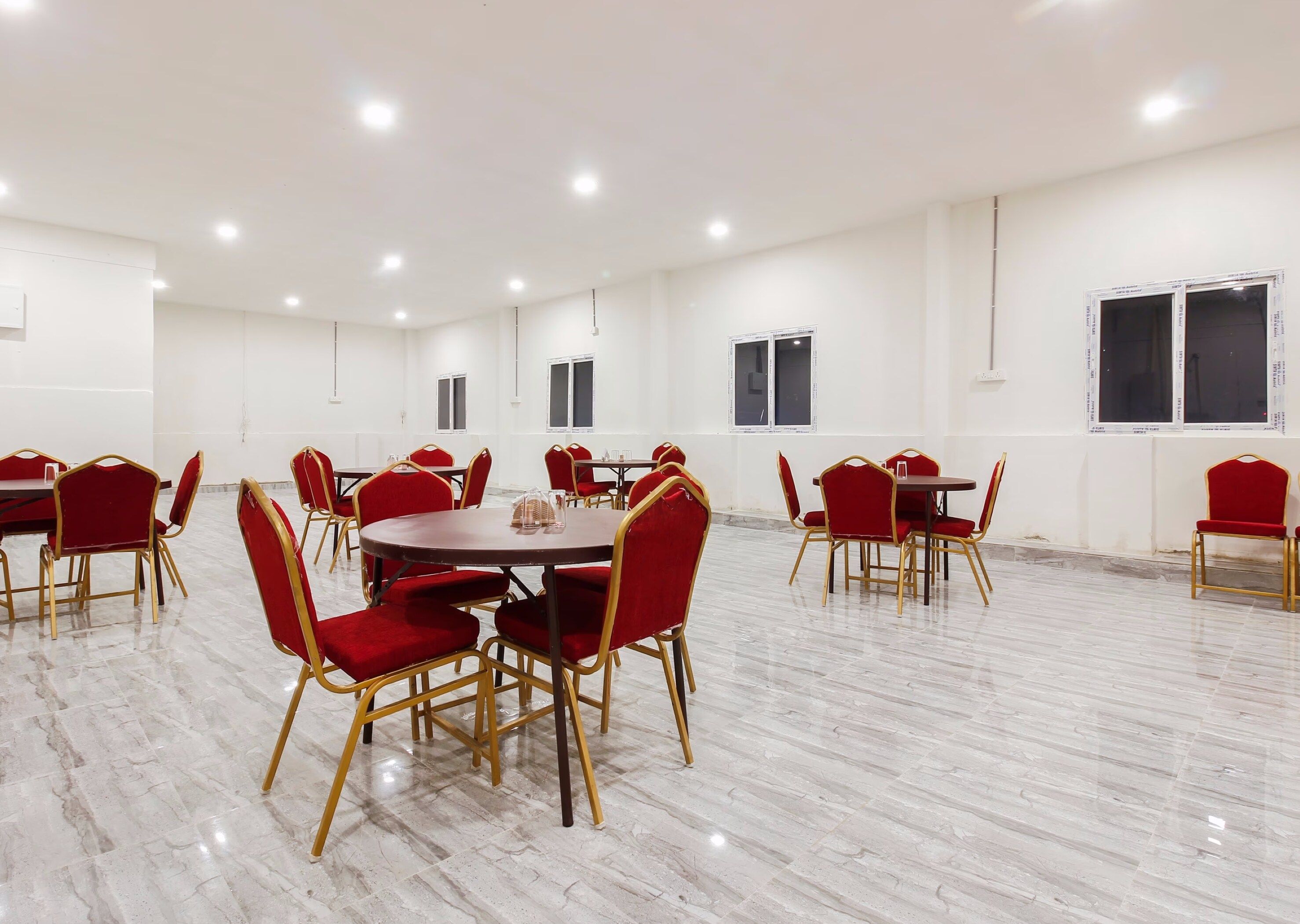 Sala de conferências com várias mesas e cadeiras, paredes brancas e piso de mármore.