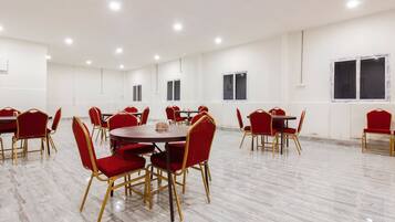 Sala de conferências com várias mesas e cadeiras, paredes brancas e piso de mármore.
