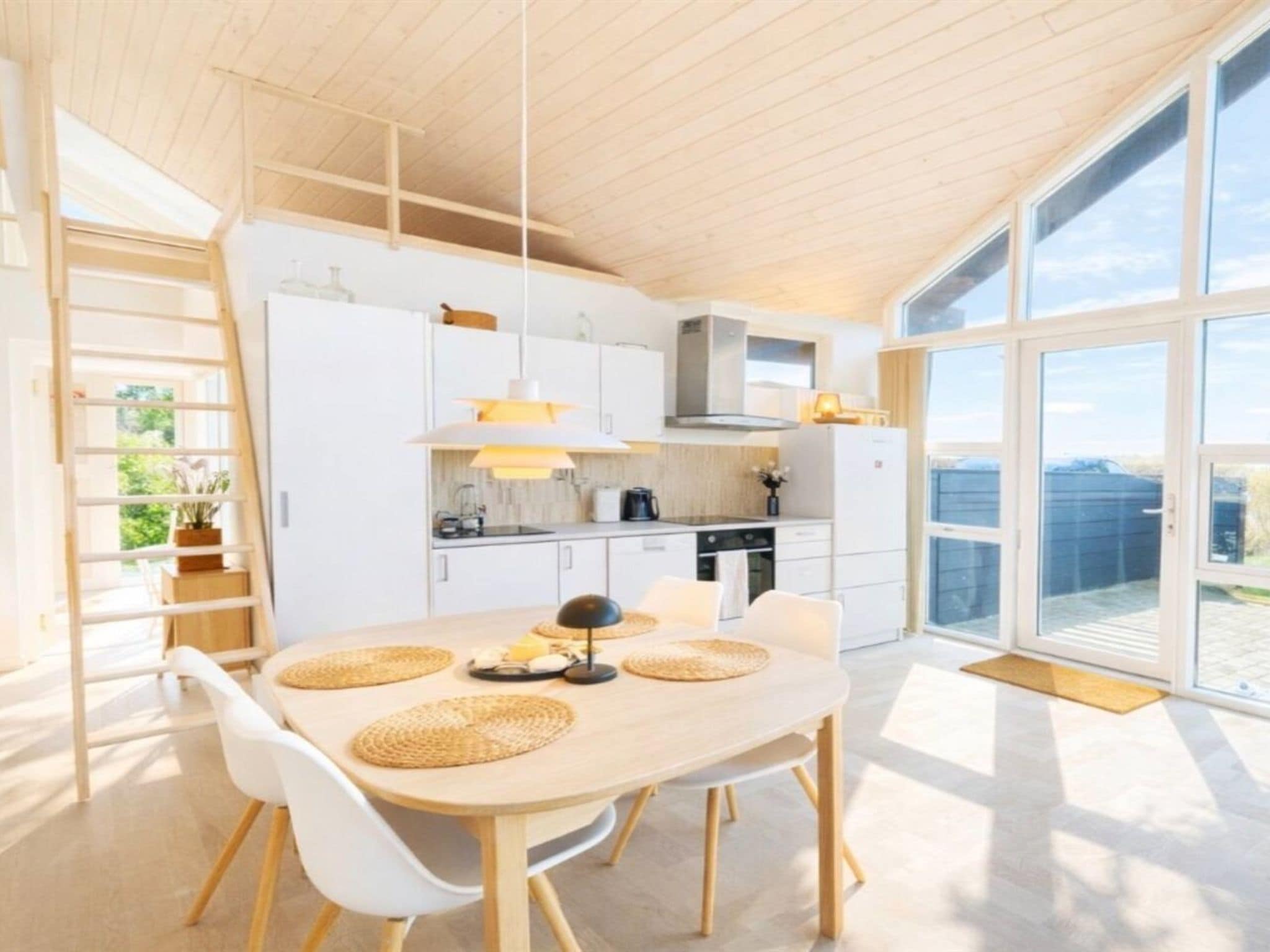 A modern kitchen with white cabinetry, a dining table with chairs, and large windows.