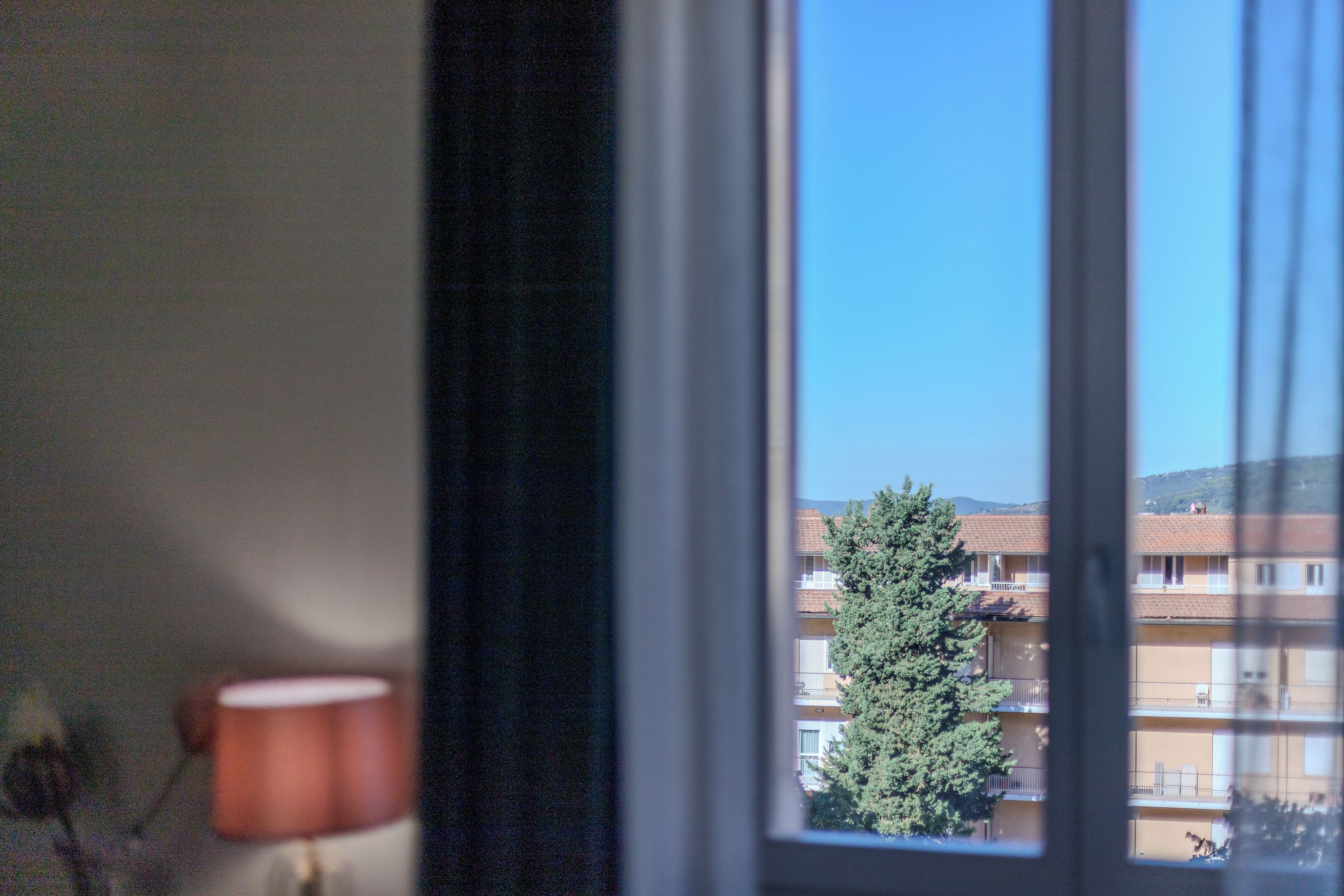 Une fenêtre donnant sur un immeuble doté de nombreux balcons, avec un arbre au premier plan.